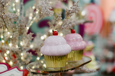 Two cupcakes are on a table. One is pink and the other is white. The pink cupcake has a cherry on topの写真素材