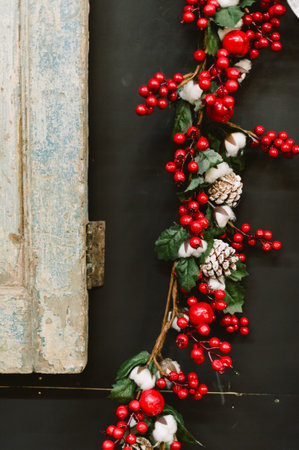 A red and white Christmas wreath with red berries and white cotton balls. The wreath is hanging on a black wallの写真素材