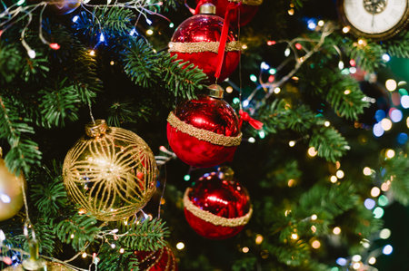 A Christmas tree with red and gold ornaments. The tree is lit up with lights. There are three red balls on the treeの写真素材