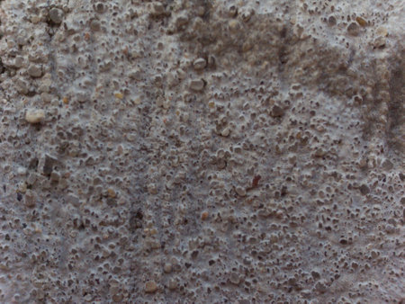 A wall with a lot of holes in it. The holes are small and scattered. The wall is made of concreteの写真素材