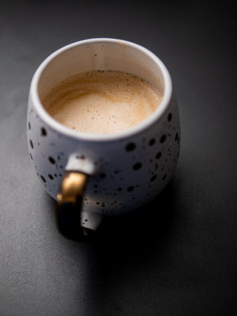A white coffee mug with a gold handle and black spots. The coffee is brown and frothyの写真素材