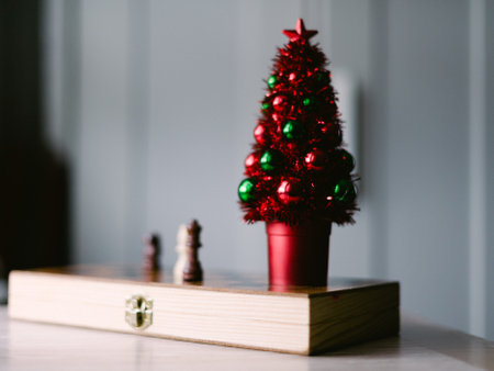 A red and green Christmas tree sits on a table next to a chess set. Scene is festive and cozy, with...