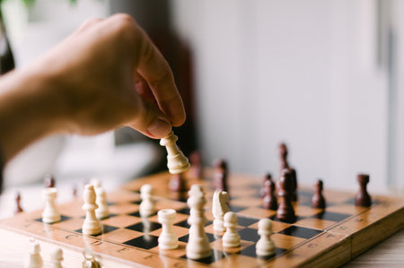 A person is playing a game of chess with a wooden board and pieces. The player is reaching for a...