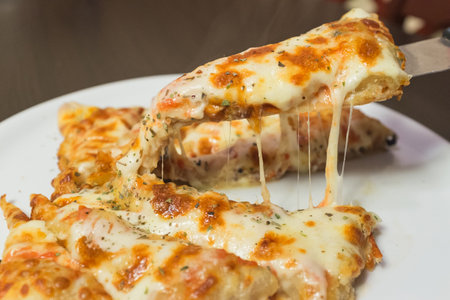 A slice of pizza with cheese on it. A knife is being used to cut the pizza. The pizza is on a white plateの写真素材