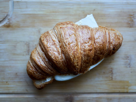 Croissant with a slice of cheese on top. The croissant is sitting on a wooden cutting boardの写真素材
