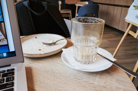 Laptop is on a table with a plate of food and a glass of milk. A fork is on the plate and a knife is on the tableの写真素材