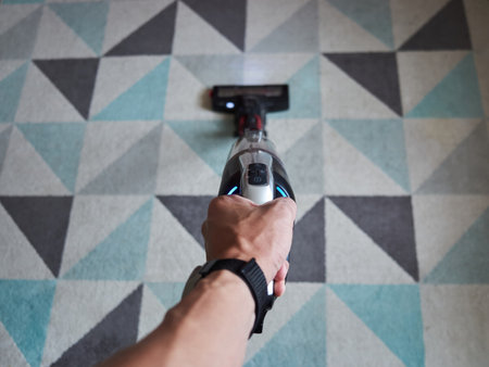 Person is holding a vacuum cleaner with a blue button on it. The image has a casual and relaxed mood, as the person is simply holding the vacuum cleaner and not in a hurryの写真素材
