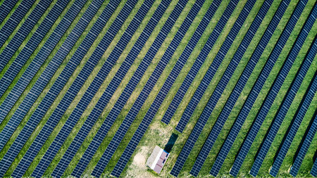 Field of solar panels with a small house in the middle. The house is surrounded by the solar panels...