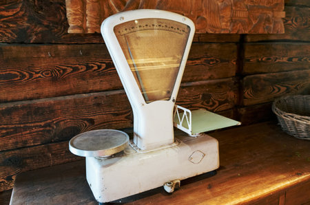 An old scale sits on a wooden table. The scale is white and has a black base. The scale is old and has a vintage look to itの写真素材