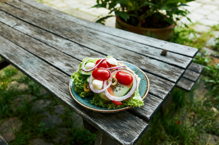 Plate of food with a variety of vegetables including lettuce, tomatoes, and onions. The plate is on a wooden table outsideの写真素材