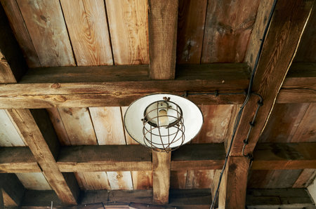 Light fixture hangs from the ceiling in a wooden room. The light fixture is a lantern with a white shade. The room has a rustic feel, with wooden beams and a wooden ceilingの写真素材