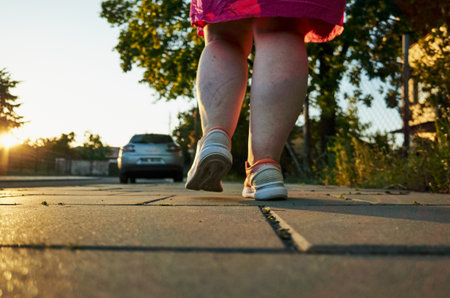 Woman in a pink dress is walking on a sidewalk. The sun is setting, casting a warm glow on the sceneの写真素材