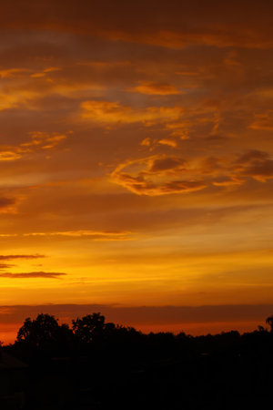 The sky is orange and the clouds are white. The sun is setting and the sky is filled with clouds. Phone wallpaper Vertical background.の写真素材