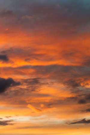 The sky is orange and the clouds are white. The sun is setting. Phone wallpaper Vertical background.の写真素材