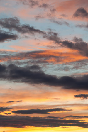 The sky is filled with clouds and the sun is setting. The sky is a mix of orange and blue colors. Phone wallpaper Vertical background.の写真素材