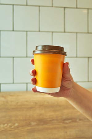 Person is holding a cup with a lid on it. The cup is orange.