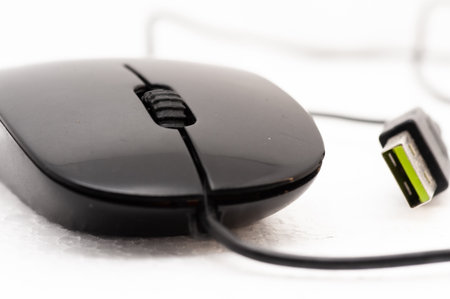 A black computer mouse with a green cord attached to it. The mouse is sitting on a white surface