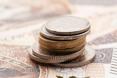 A stack of coins on top of a piece of paper. The coins are silver and gold. The paper is brown and...