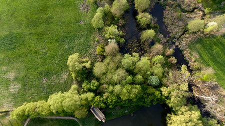 Green field with trees and a path. The trees are in various stages of growth, with some in full bloom and others still budding. The grass is lush and green, and the path winds through the trees. Drone viewの写真素材