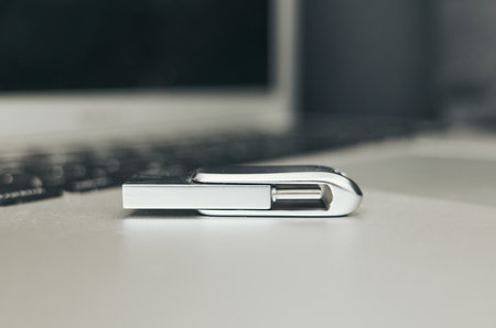 Silver USB flash drive sits on a white laptop keyboard. The flash drive is open and the keyboard is turned offの写真素材