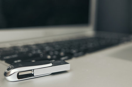 Silver USB flash drive sits on a laptop keyboard. The flash drive is small and silver, and it is likely used for storing and transferring dataの写真素材