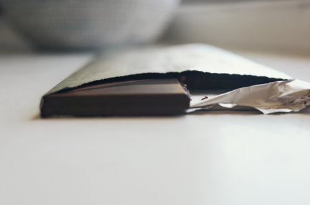 Chocolate bar is opened and laying on a table. The foil wrapper is torn and the chocolate is exposed
