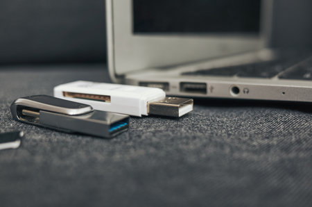 Laptop with a white USB drive and a black USB drive on top of it. The laptop is open and the USB drives are attached to itの写真素材