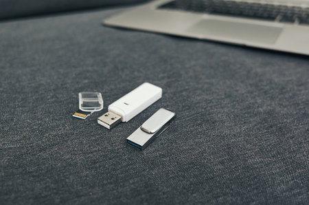 White USB drive sits on a blue couch next to a laptop. The USB drive is open and the laptop is turned offの写真素材