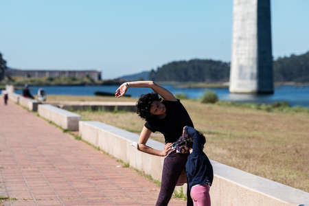 mother and daughter doing pilates exercises in a riverside area