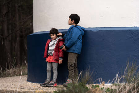 a boy and girl Caucasian play on the blue and white wall of a lighthouse.の写真素材