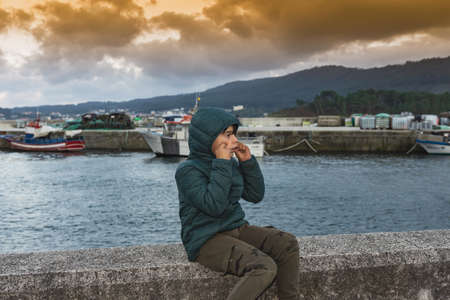 portrait of a small boy sitting on the harbour wall.の写真素材