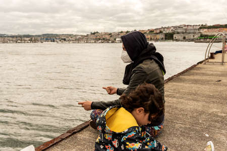 Caucasian mother and daughter sit for fishing in harbourの写真素材