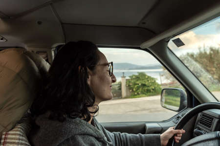 Caucasian woman with dark hair and glasses drives a camper van
