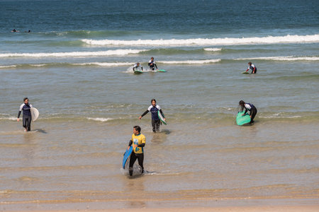 surf lessons. A group of young boys and girls in white t-shirts come out of the sea with the...