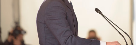 unrecognizable businessman in blue suit speaks into microphones at eventの写真素材