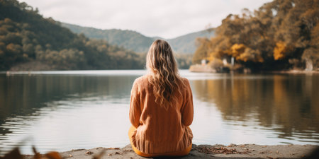 a person sitting on a rock looking at a body of waterの素材