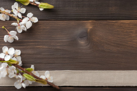 a branch with white flowers and green leaves on a wooden surfaceの素材