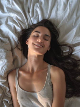 Young woman smiling while lying down on a bed with eyes closedの素材