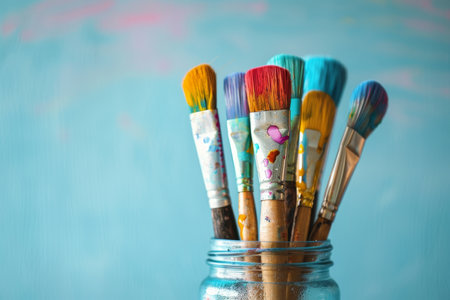 Colorful paintbrushes in a glass jar against a vibrant backgroundの素材
