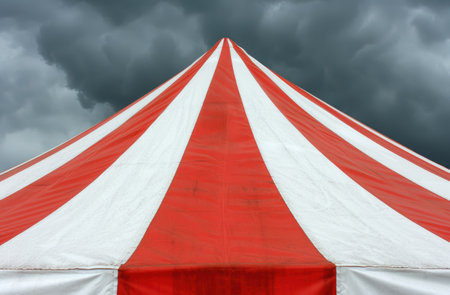 Dramatic storm clouds over a red and white circus tentの素材