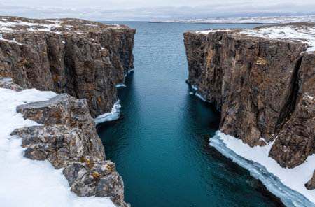 Dramatic rocky cliffs and turquoise waters in a snowy landscapeの素材