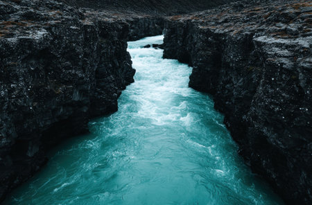 Powerful turquoise river flowing through rugged black cliffsの素材