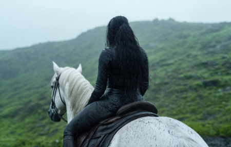 person riding white horse in rainy mountain landscapeの素材