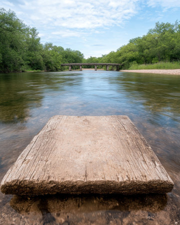 Rustic wooden platform in shallow river with old bridge in backgroundの素材