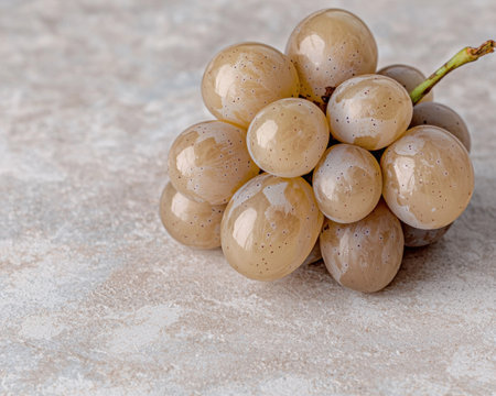Close-up of a cluster of ripe, pale beige grapes on a light beige textured surface.の素材