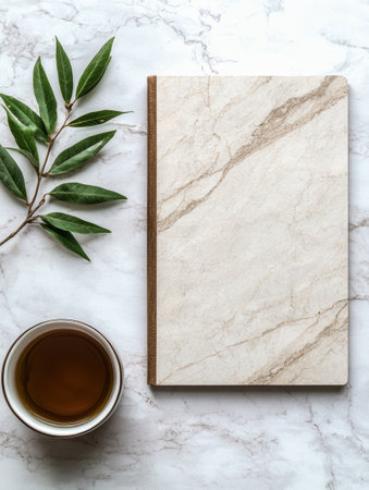 Flatlay of a marble notebook, teacup, and green leaves on a marble backgroundの素材