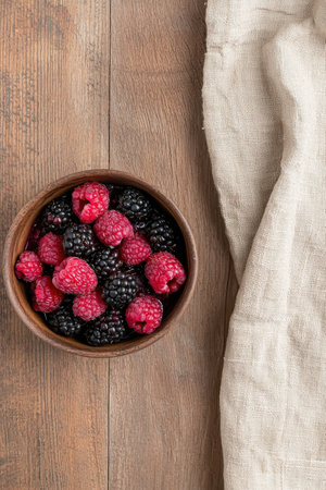 Fresh raspberries and blackberries in a wooden bowl on a rustic wooden tableの素材