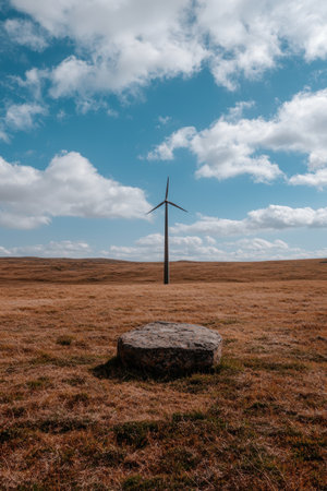 Single wind turbine in a vast field under a cloudy skyの素材