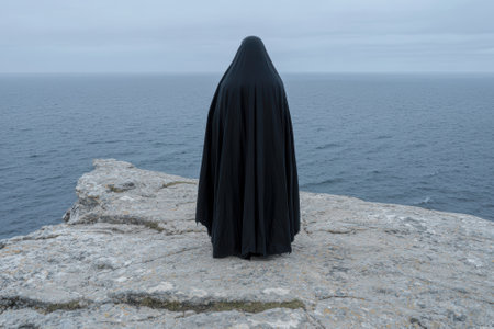 Mysterious figure in black robe overlooking the ocean from a cliffの素材