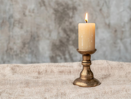 Burning candle on antique brass candlestick holder on linen fabricの素材